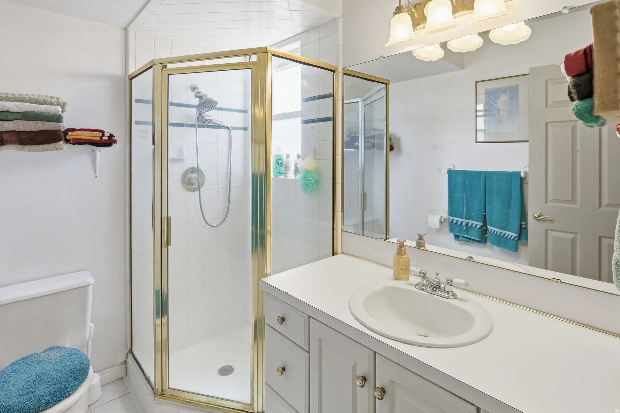 Bathroom featuring a corner shower with a gold-toned frame, an integrated vanity sink, a broad wall-mounted mirror, and a multi-light fixture