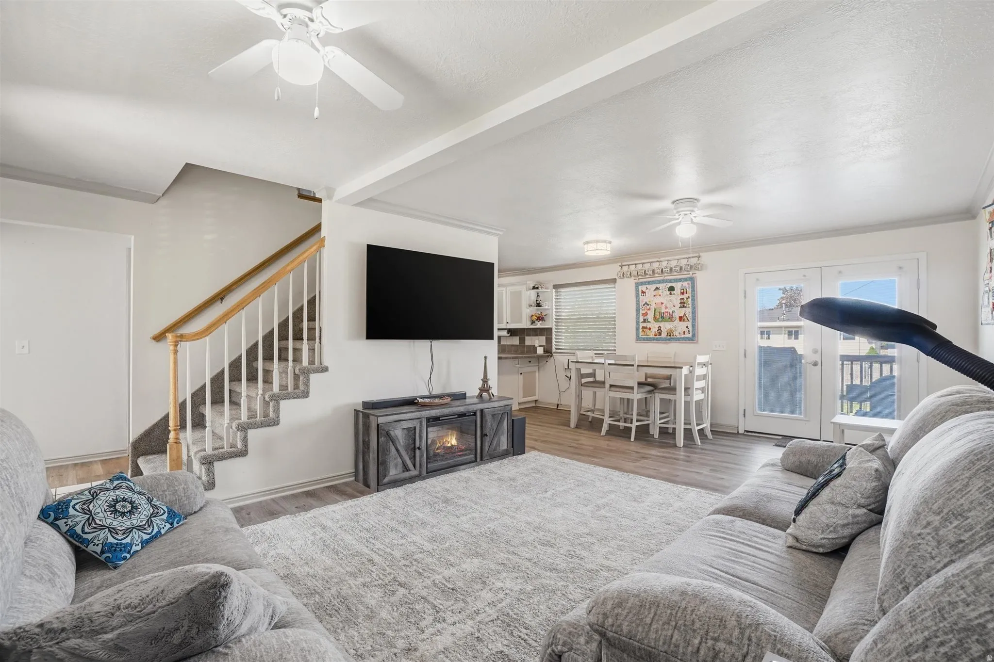 Open-concept living area with wood-finish flooring, a contemporary electric fireplace console, and multiple ceiling fans