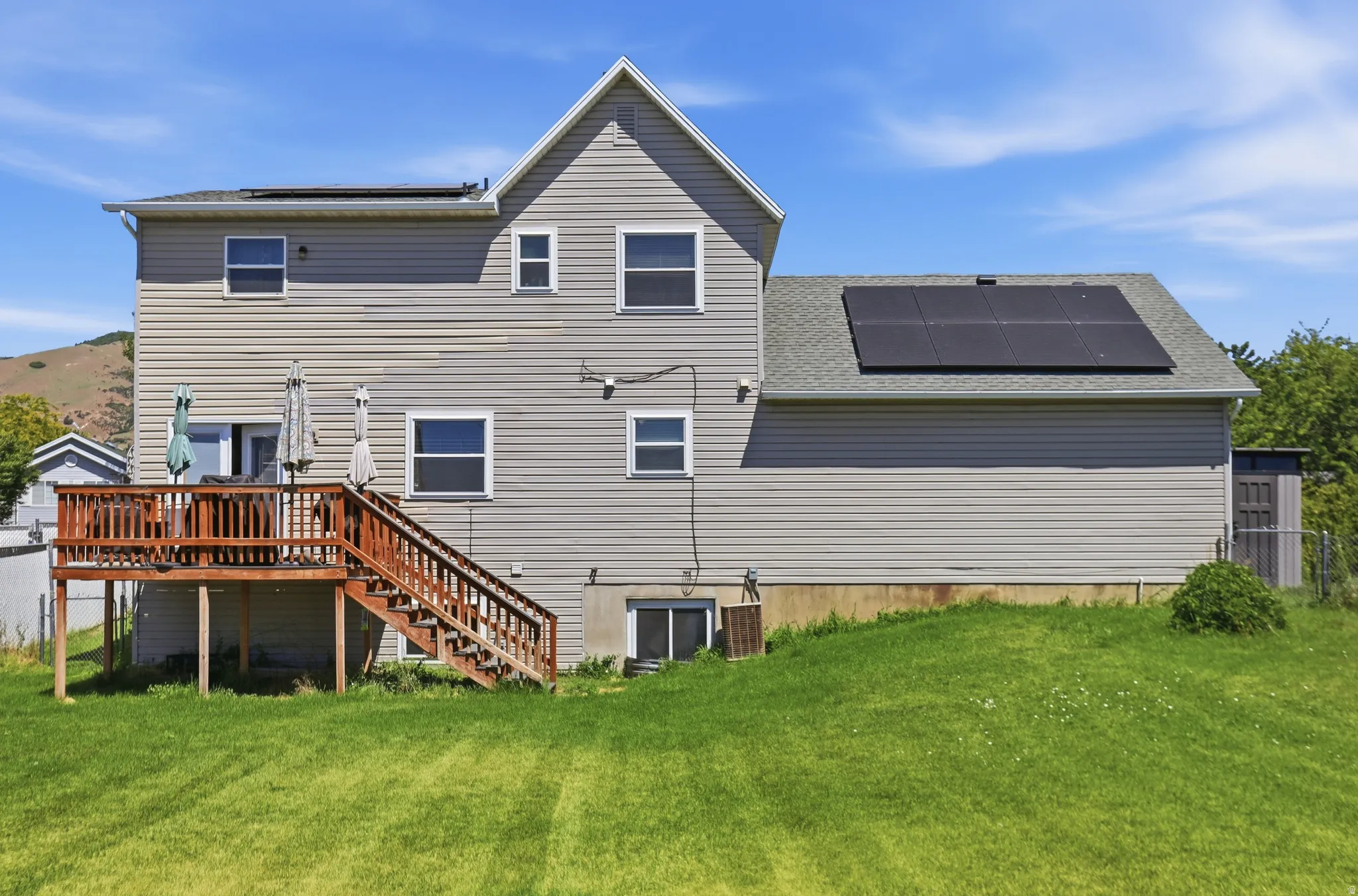 Rear exterior featuring a multi-level wood deck with stairs to the lawn, light gray siding, and roof-mounted solar panels
