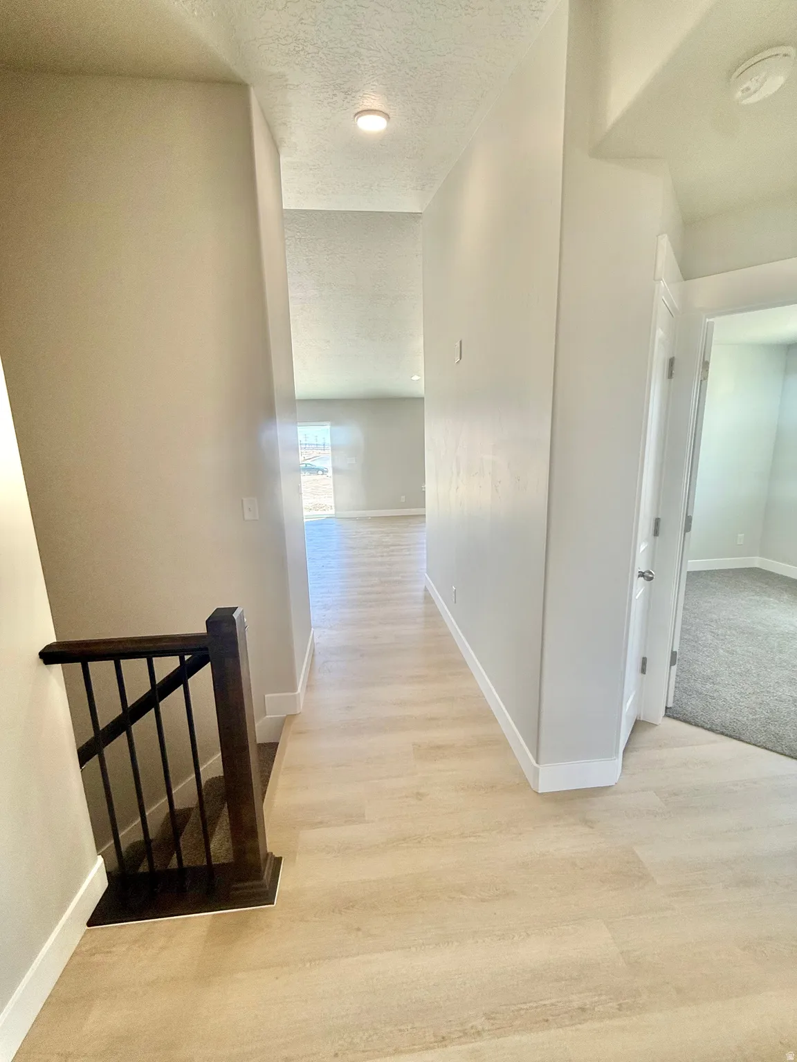 Inviting hallway with light wood-finish flooring, crisp white baseboards, and neutral wall tones