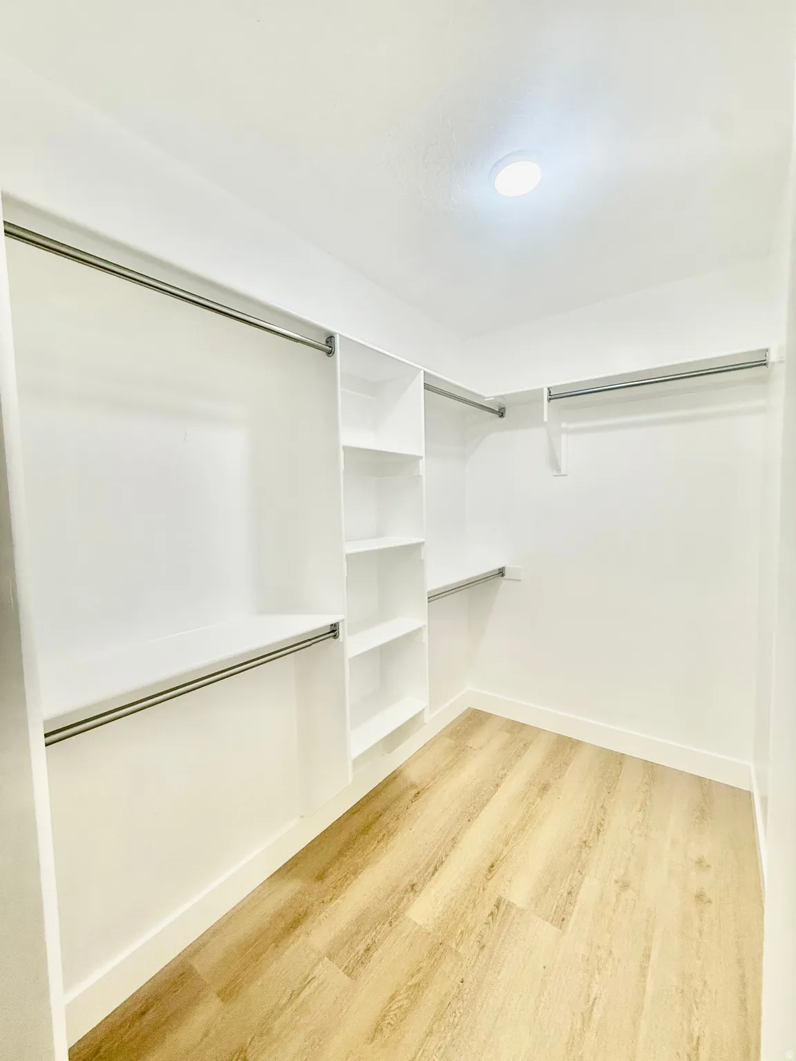 Walk-in closet featuring wood-finish flooring, recessed lighting, white built-in shelving, and multiple clothing rods for organized storage