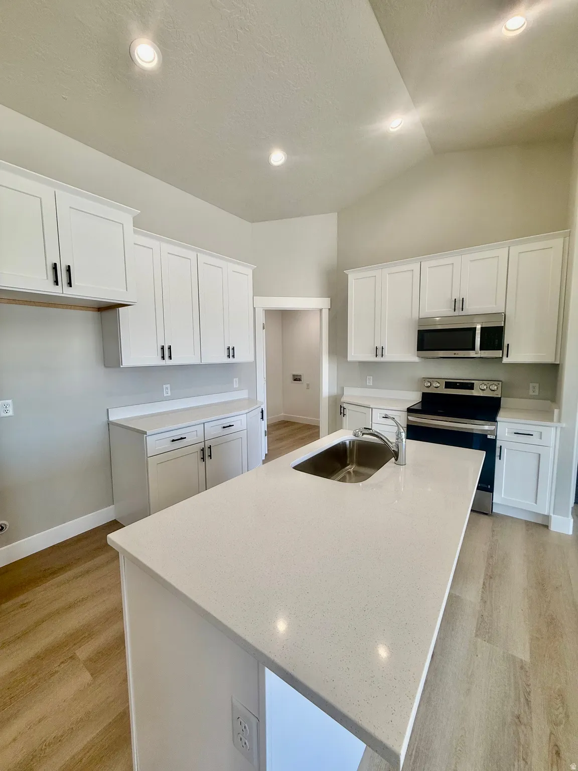Kitchen featuring a central island with an undermount sink, light-toned countertops, and wood-finish flooring