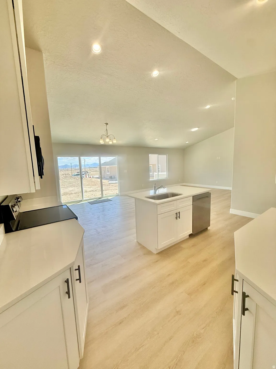 Open-concept living area featuring a kitchen island with integrated sink, stainless steel dishwasher, light wood-finish flooring, and recessed ceiling lighting