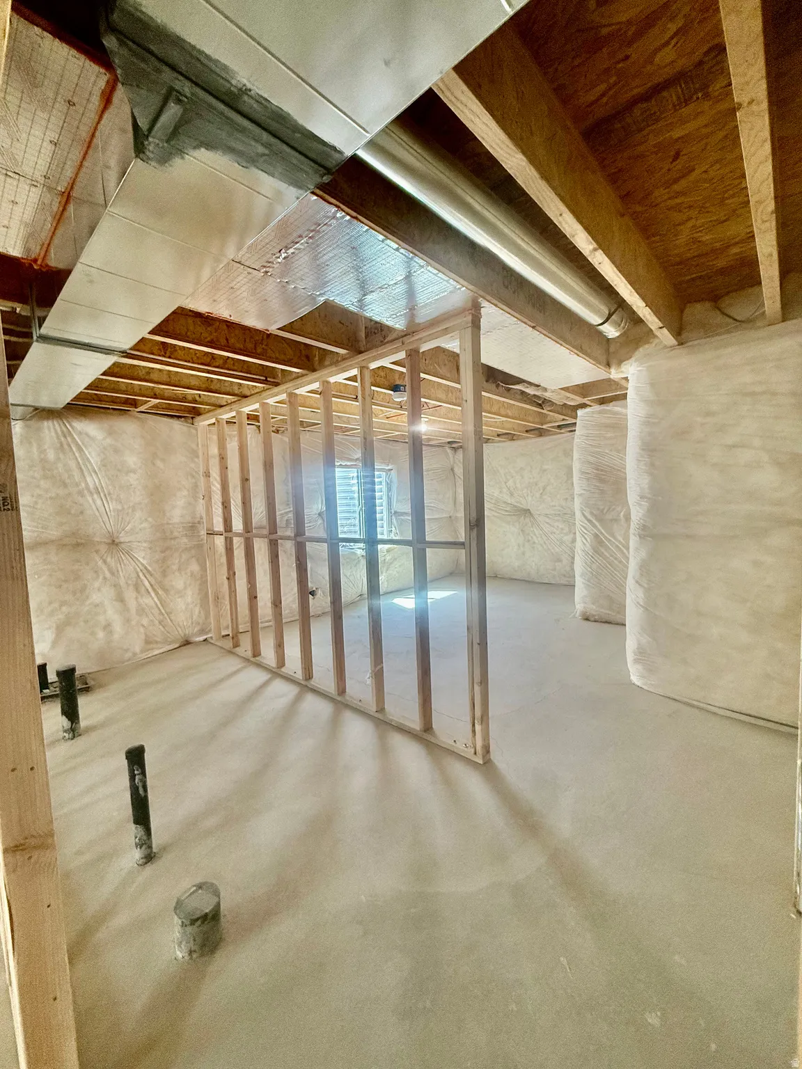 Unfinished basement featuring exposed wood joists and subfloor, partial wood framing for future rooms, and concrete flooring
