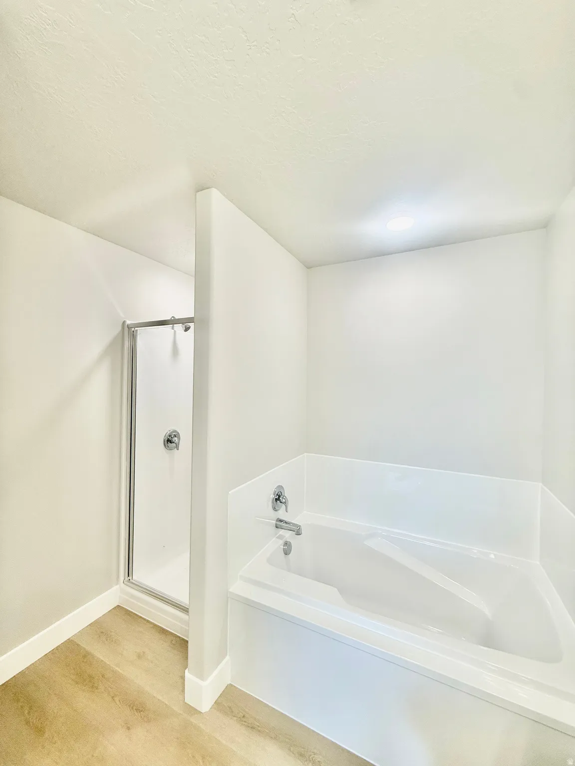 Bathroom featuring a built-in soaking tub, a separate shower with a glass enclosure, wood-finish flooring, and white baseboards