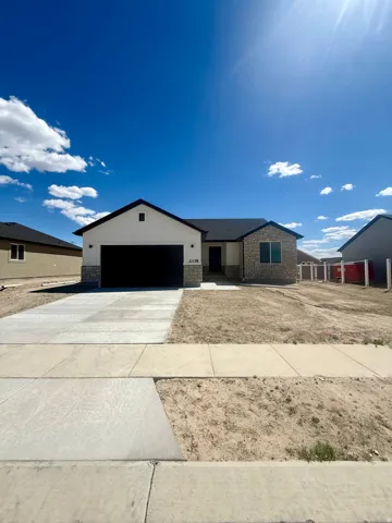 Contemporary ranch-style home featuring a two-car garage, partial stone facade, covered entry, and a concrete driveway
