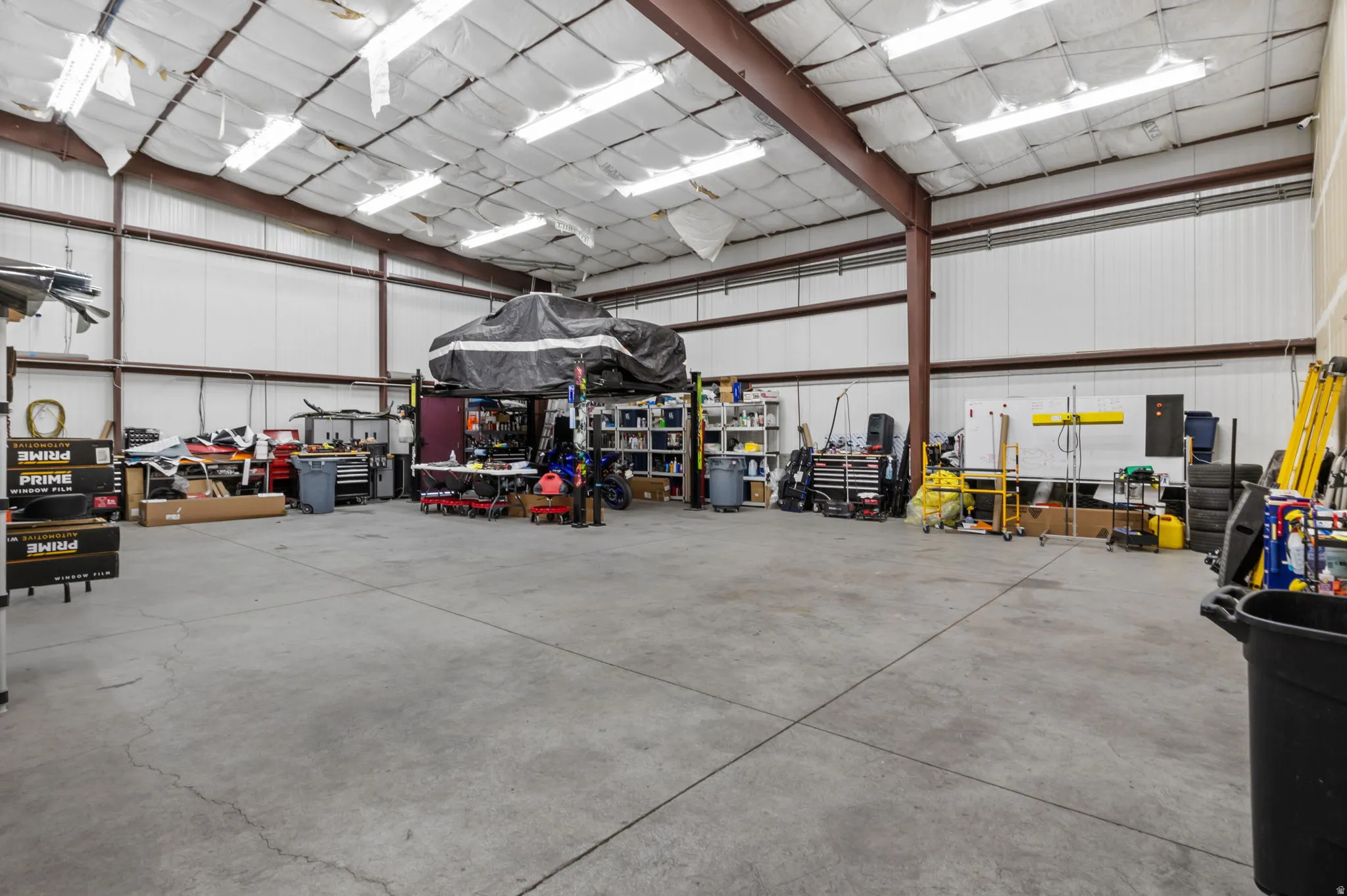 Spacious commercial warehouse featuring a high ceiling, polished concrete flooring, metal beam construction, extensive fluorescent lighting, and white corrugated metal walls