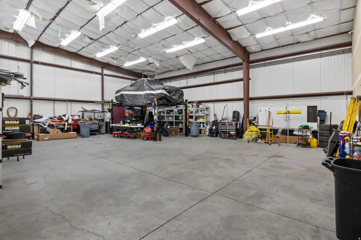 Spacious commercial warehouse featuring a high ceiling, polished concrete flooring, metal beam construction, extensive fluorescent lighting, and white corrugated metal walls