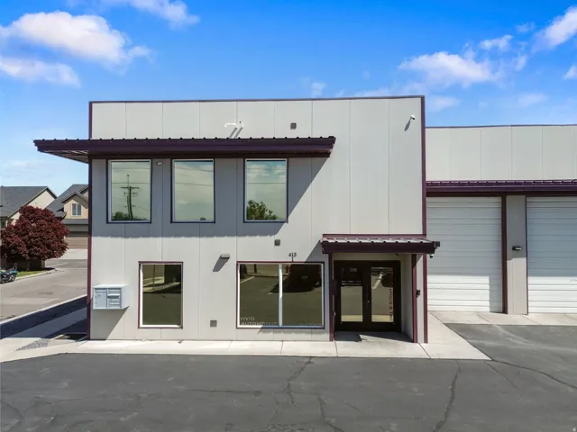 Modern commercial building featuring a light gray facade, dark trim accents, multiple large windows, a covered entrance, and an attached garage bay