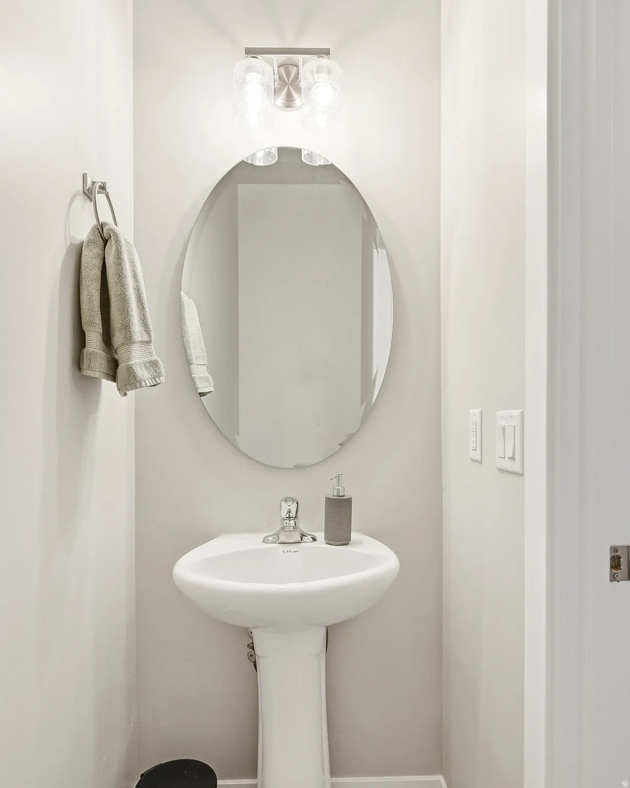 Pedestal sink with chrome faucet, complemented by an oval mirror
