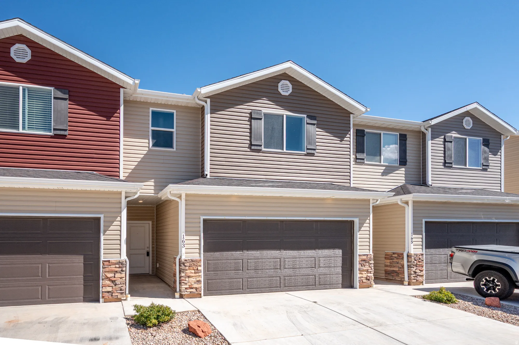 Contemporary multi-level townhome featuring a two-car garage, stone accents, horizontal siding, black window shutters, and a covered entry