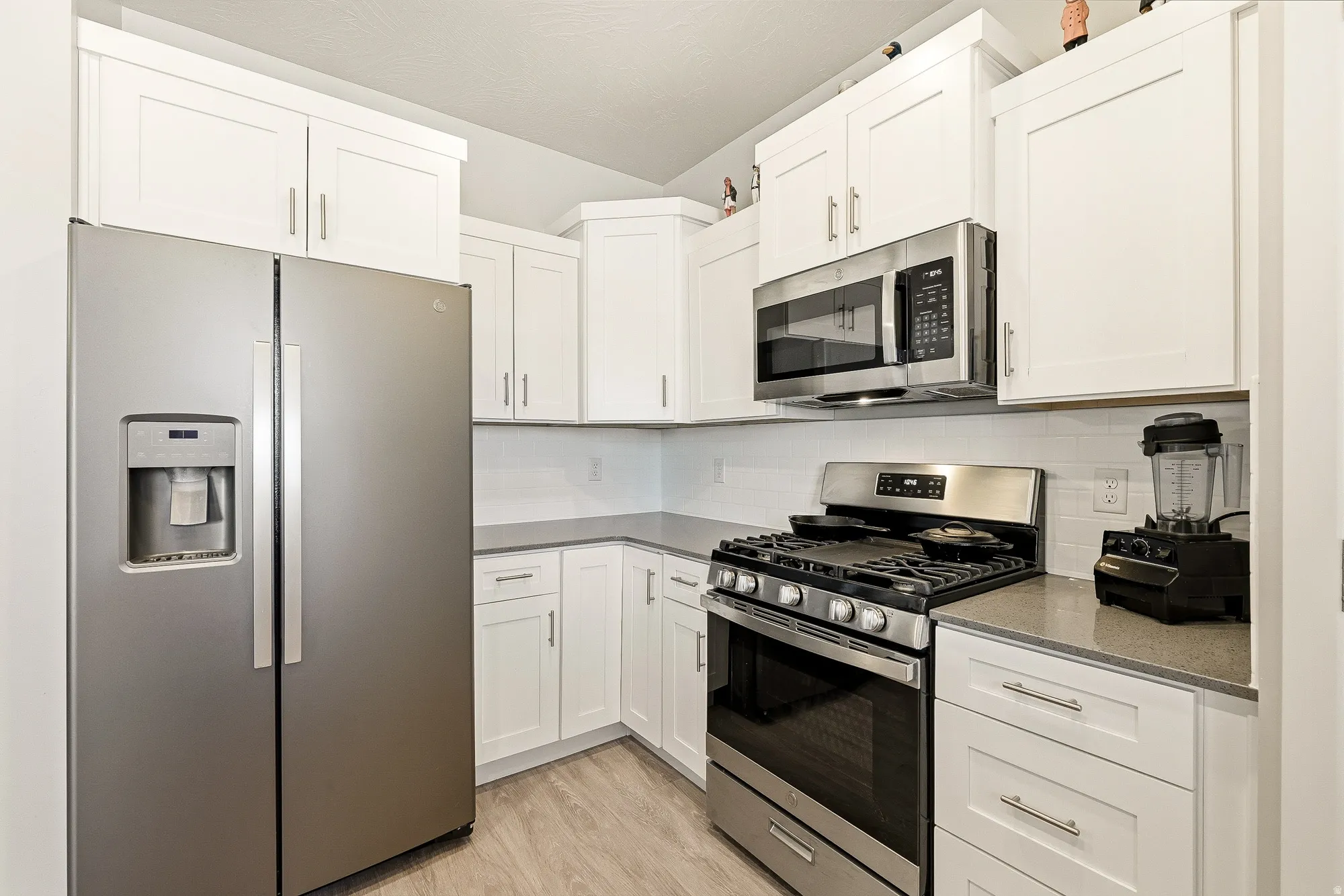 Corner kitchen featuring white cabinetry with silver hardware, stainless steel appliances, gray countertops, and wood-finish flooring