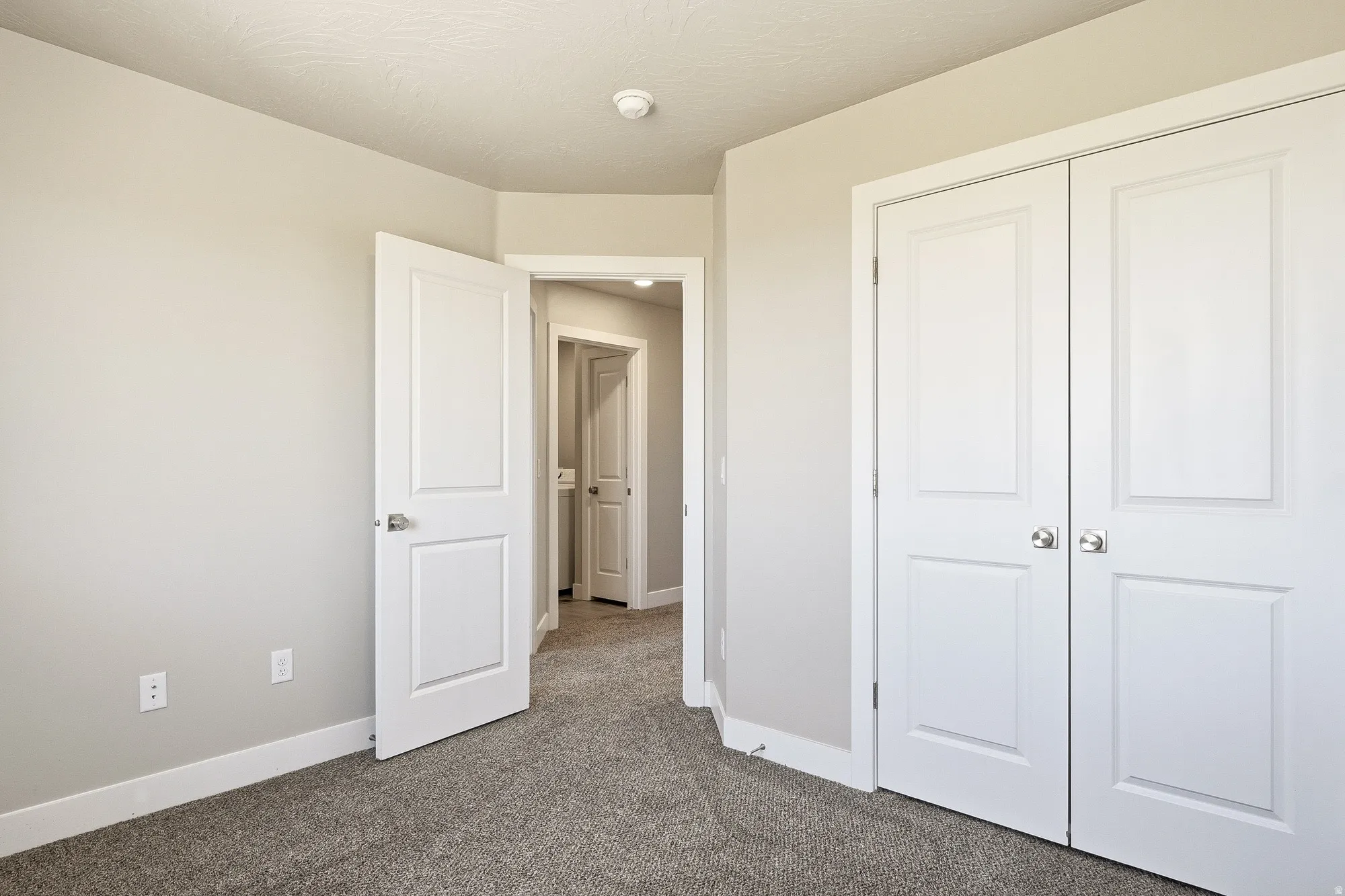 Spacious room featuring neutral paint, gray carpet, white baseboards, and a double-door closet with brushed nickel hardware