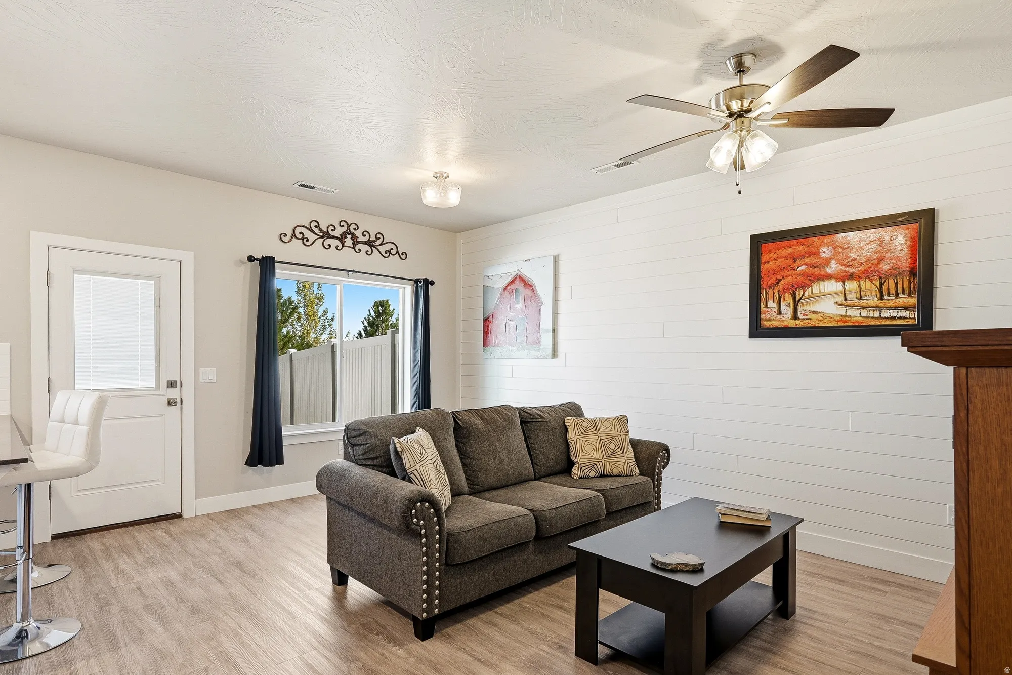 Living area featuring light wood-finish flooring, a contemporary ceiling fan with integrated lighting, and a prominent shiplap accent wall