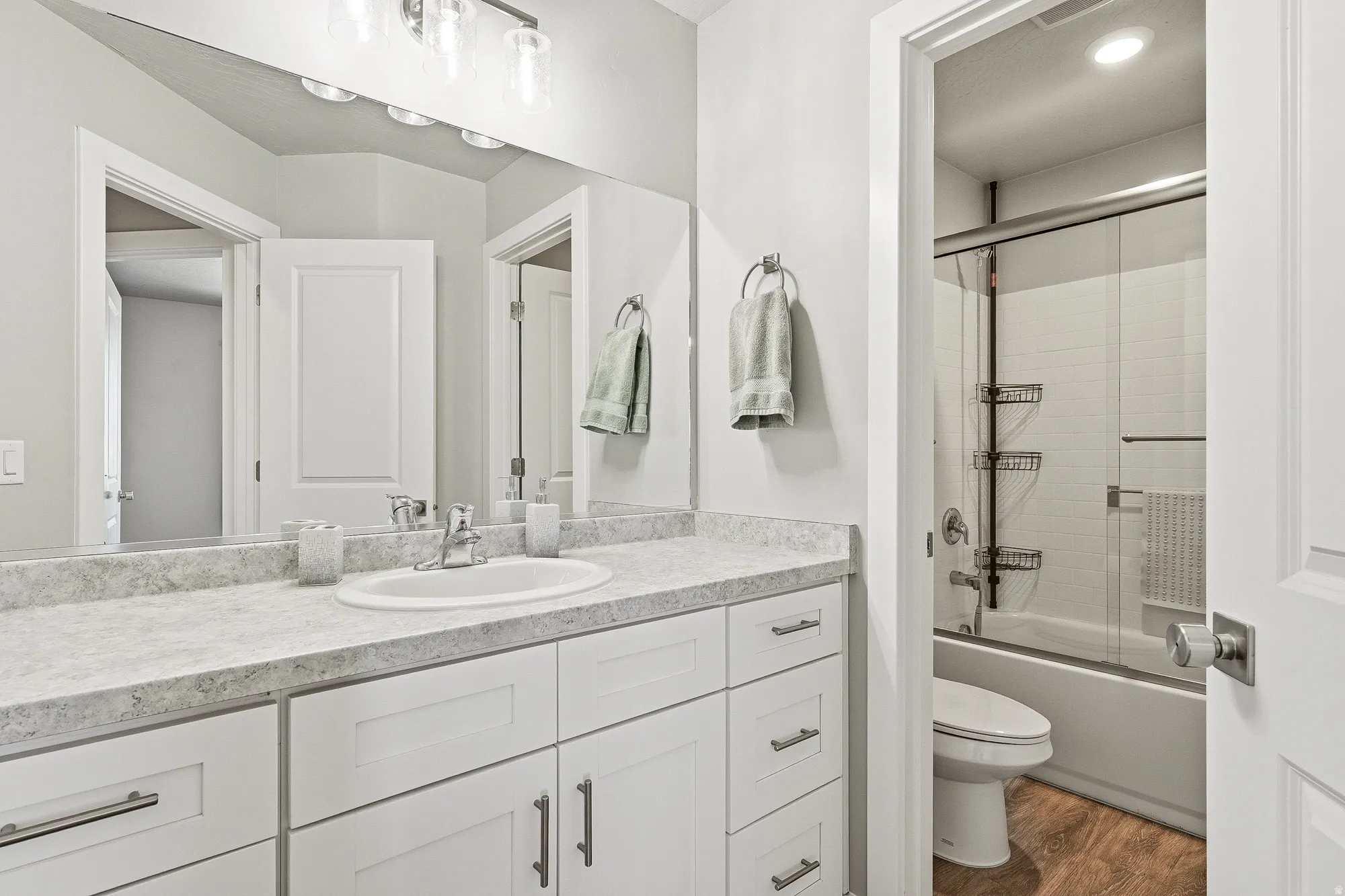 Contemporary bathroom featuring a spacious vanity with white cabinetry, a light-colored countertop, and a large wall-mounted mirror