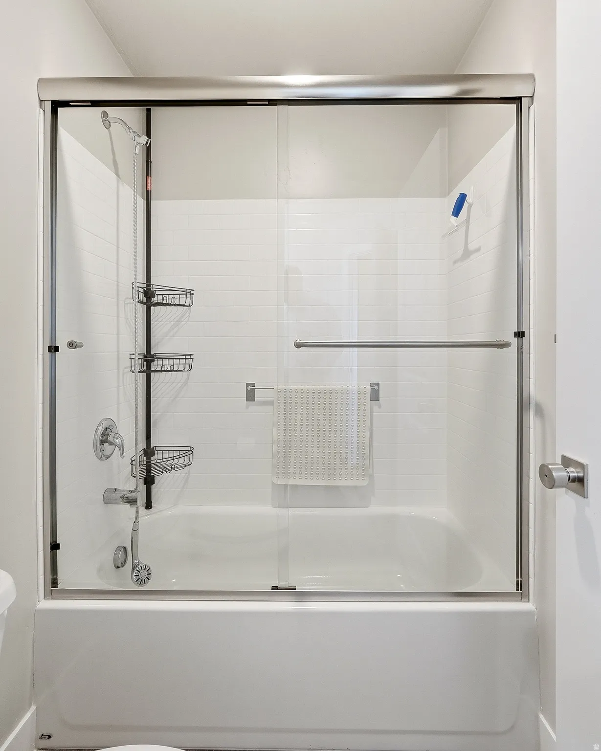 Bathtub and shower combination featuring a sliding glass door enclosure, white subway tile surround, and brushed nickel fixtures