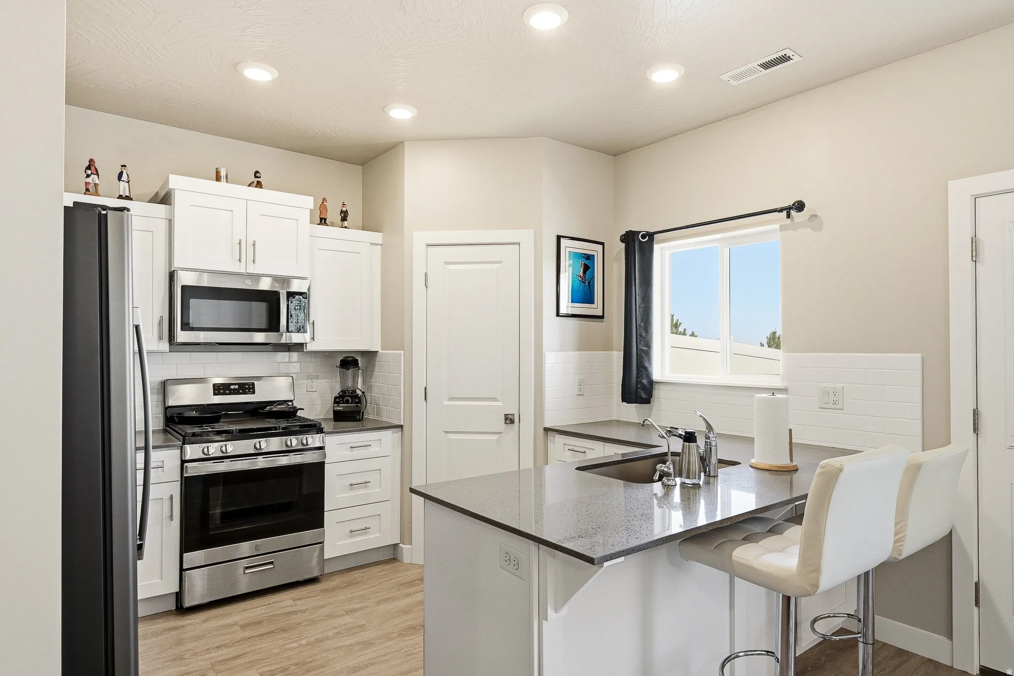 Contemporary kitchen featuring recessed lighting, white cabinetry, stainless steel appliances, dark countertops, and wood-finish flooring