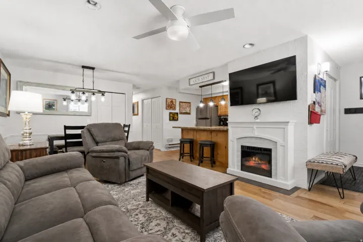 Living room with light wood finished floors, a glass covered fireplace, a ceiling fan, and recessed lighting