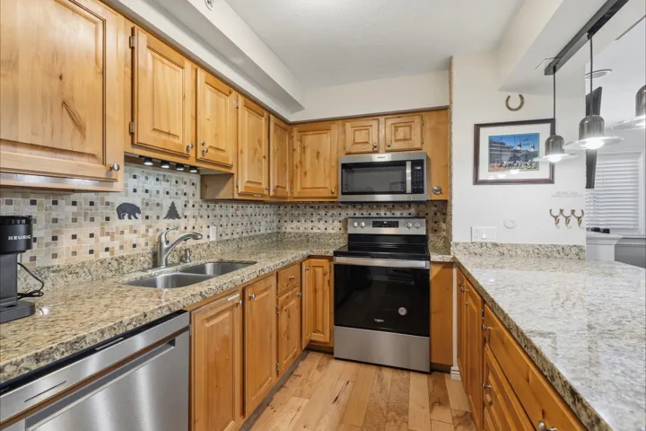 Kitchen with stainless steel appliances, light wood-style flooring, light stone countertops, backsplash, and pendant lighting