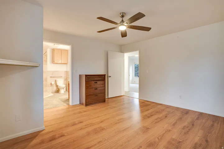 Spacious room with wood-finish flooring, a contemporary ceiling fan with integrated lighting, and white wall finishes