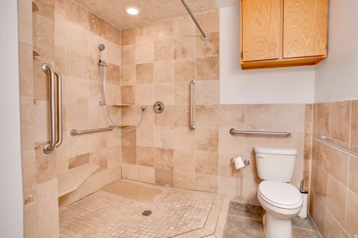 Walk-in shower with tiled walls and floor, featuring a built-in bench and multiple grab bars