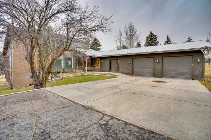 Exterior facade featuring a combination of brick and siding, a large concrete driveway, and an attached three-car garage with a metal roof