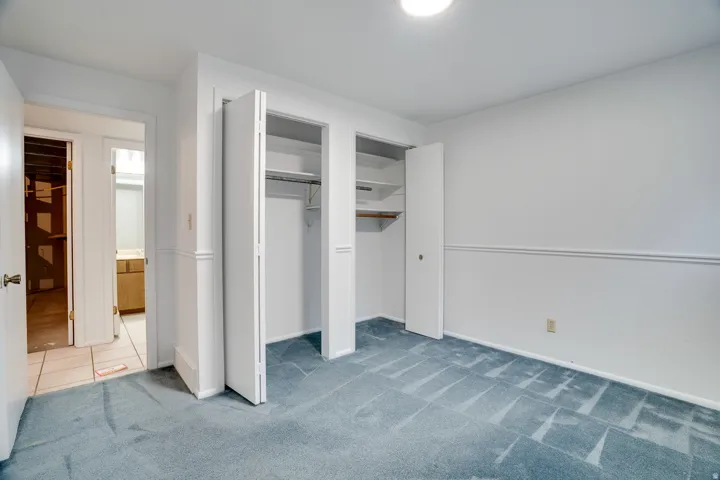 Room with plush blue carpet, white walls with wainscoting, and two bi-fold door closets featuring shelving and hanging rods