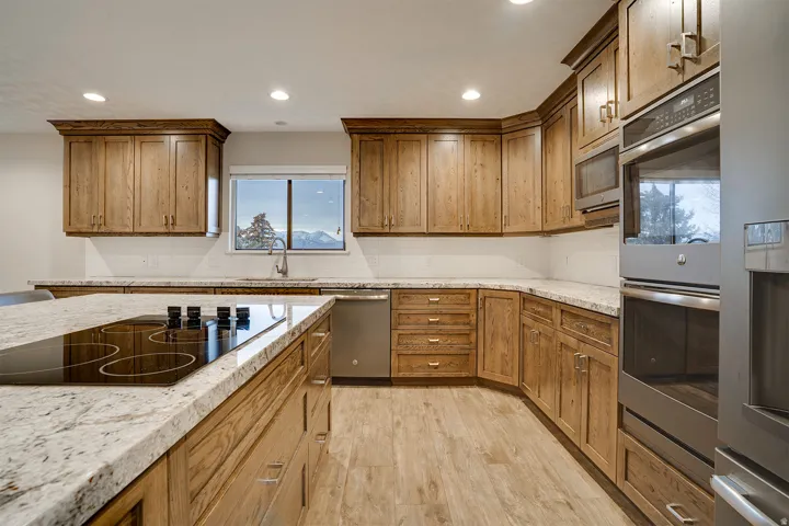 Gourmet kitchen featuring a built-in cooktop on a large island, stainless steel double ovens, custom wood cabinetry, granite countertops, and a subway tile backsplash