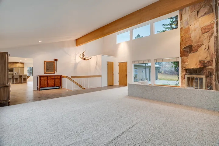 Spacious living area featuring a stone fireplace, vaulted ceilings with exposed wood beams, and large windows