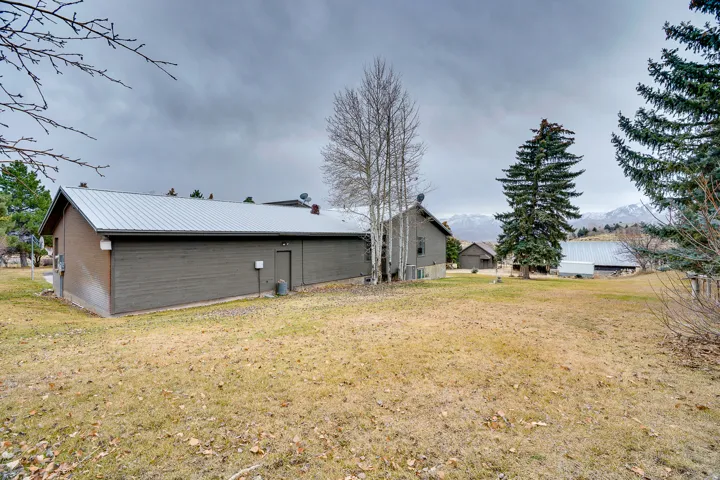 Spacious outdoor area featuring a manicured lawn, established pine trees, and distant mountain scenery