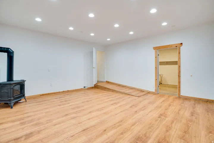 Spacious room featuring wood-finish flooring, recessed ceiling lighting, and a freestanding wood-burning stove with a glass door