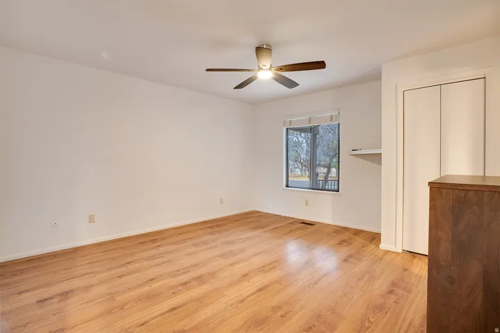 Spacious room featuring wood-finish flooring, a ceiling fan with integrated lighting, and a window with exterior visibility