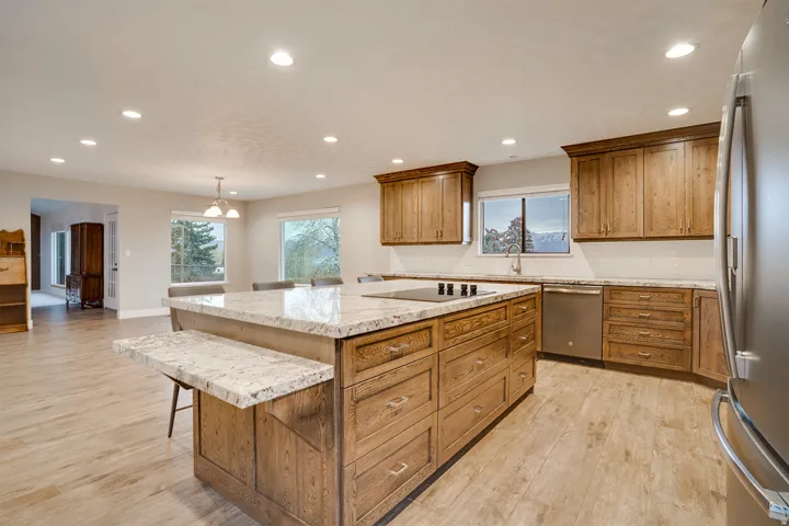 Spacious kitchen featuring a large central island with an integrated cooktop and an extended countertop, wood-finish flooring, ample wood cabinetry, stainless steel appliances, and recessed lighting