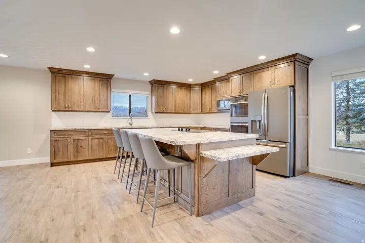 Spacious kitchen featuring custom wood cabinetry, light-toned countertops, stainless steel appliances, and a large central island with seating