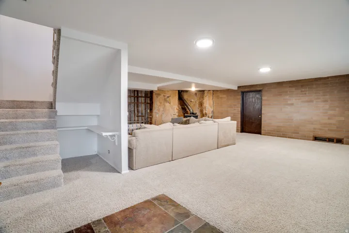 Spacious carpeted room featuring a built-in desk under the staircase, a stone accent wall, and a brick wall