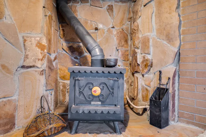 Cast iron wood-burning stove with a metal flue pipe, set against a stone wall