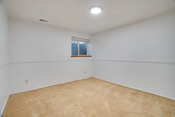 Carpeted room with a flush-mount ceiling light, a window with a white frame and blinds, and white walls featuring a chair rail