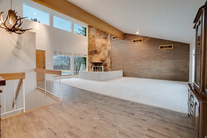 Vaulted living space featuring a stone fireplace with a raised hearth, wood-finish flooring, and high transom windows