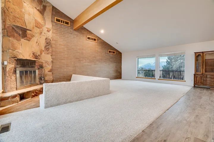 Spacious living area featuring a stone fireplace, vaulted ceilings with wood beams, and a brick accent wall