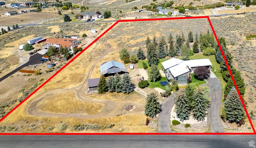 Expansive property featuring a main residence with a light-colored roof, multiple outbuildings, mature evergreen trees, and a developed driveway system