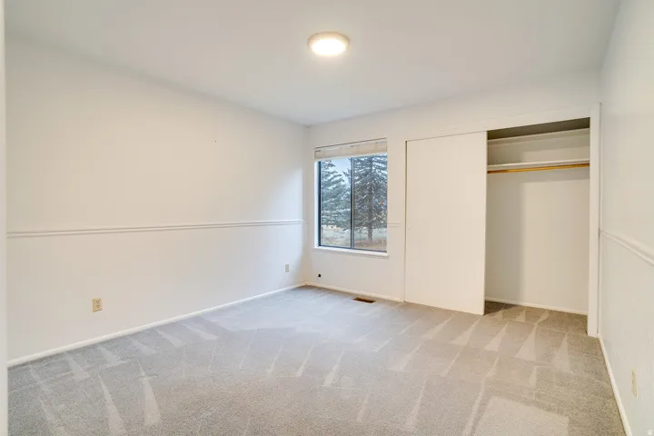 Bright interior space featuring light gray patterned carpeting, a large window, and a built-in closet with sliding doors