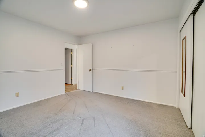 Neutral-toned room featuring a single overhead flush-mount light fixture, light gray carpeting, white walls, and white chair rail molding
