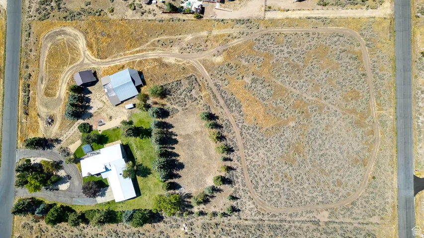 Expansive property featuring a main residence with a white roof, a separate outbuilding, a manicured green lawn area, and extensive undeveloped acreage with natural vegetation