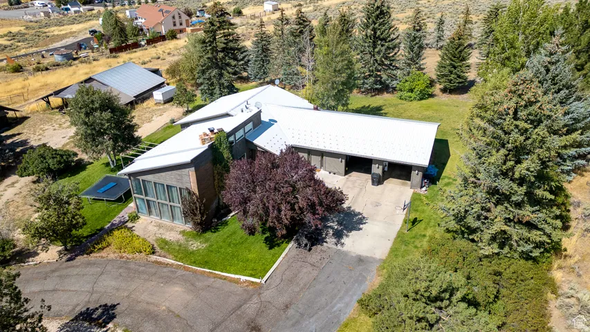 Expansive property featuring a contemporary residence with a multi-car garage, surrounding mature trees, a manicured lawn, and a paved driveway