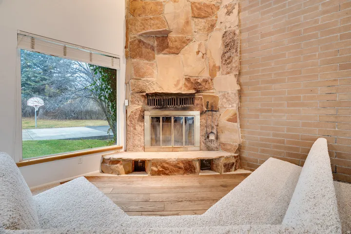 Stone-faced fireplace with a metal insert and hearth seating, complemented by a large window with wood trim