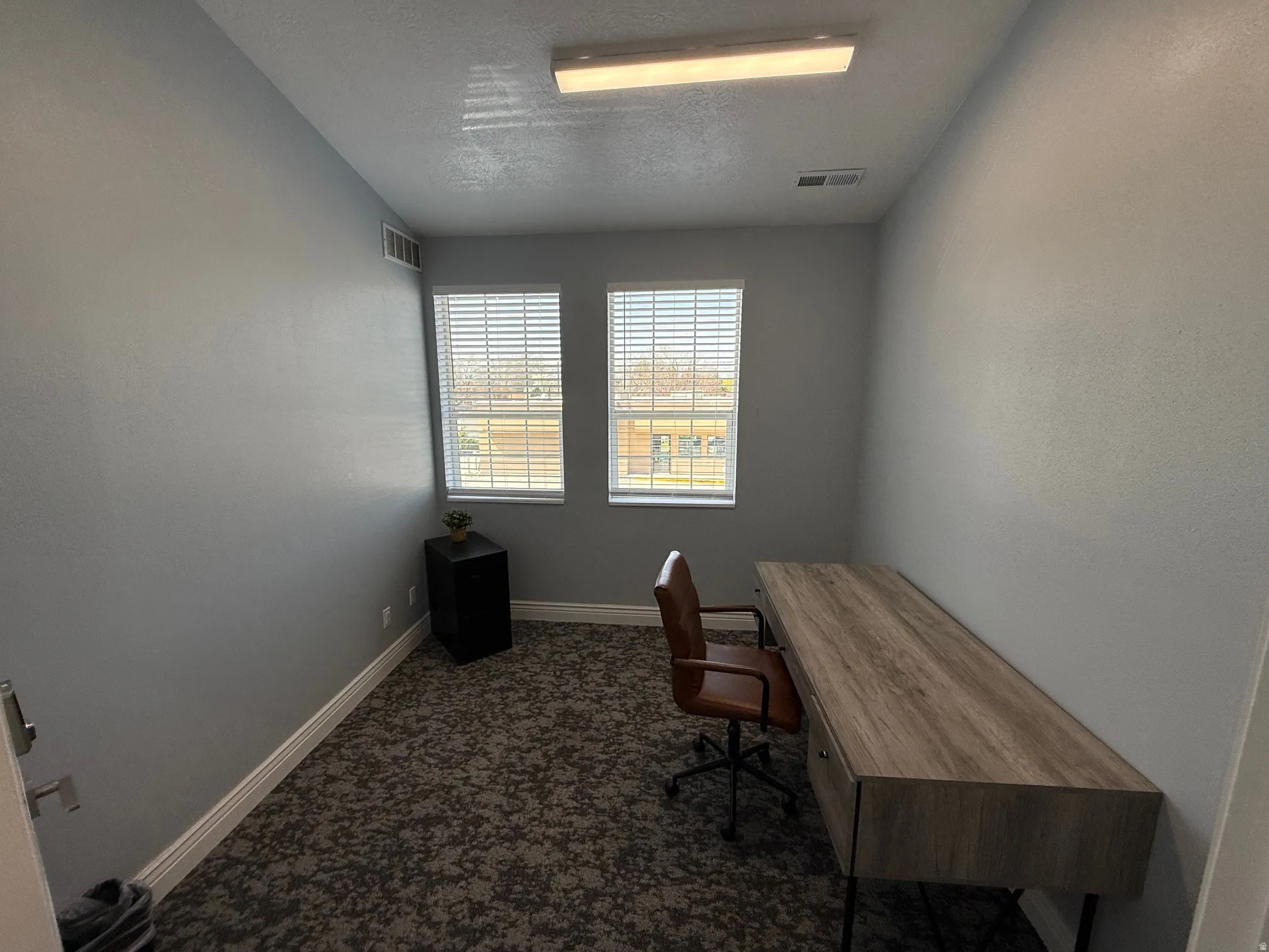 Room featuring light gray walls, patterned carpet flooring, and two windows with blinds