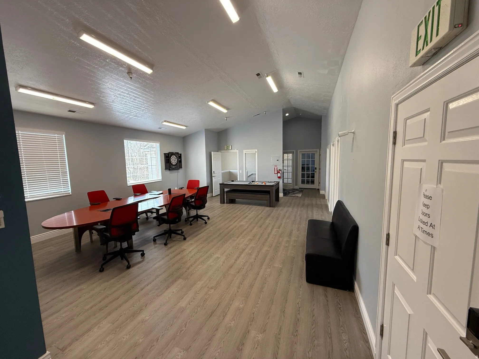 Spacious common area featuring wood-finish flooring, a vaulted ceiling, multiple windows with blinds, and recessed lighting