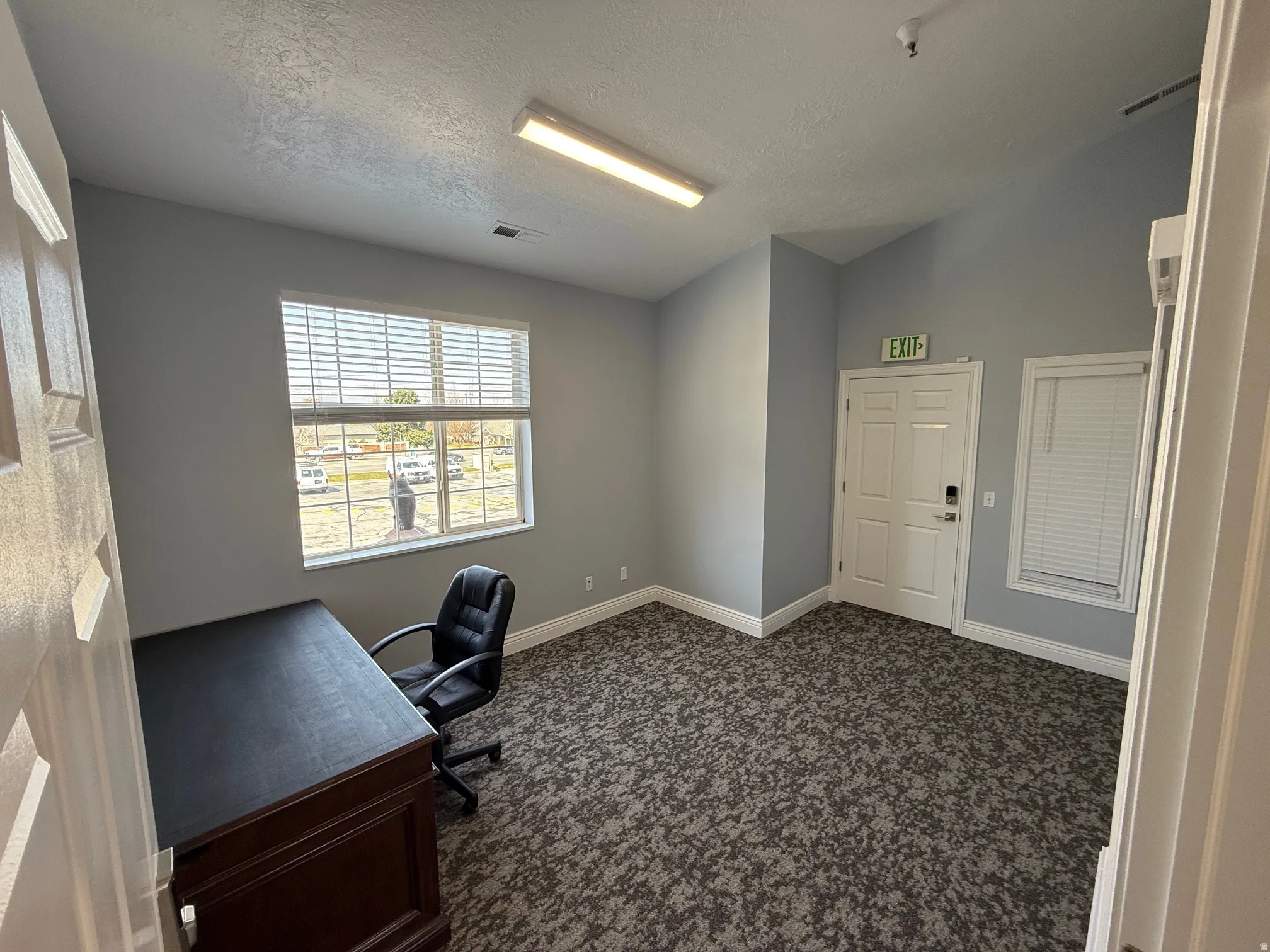 Spacious room with gray textured carpeting, a large window with white blinds, and light gray painted walls