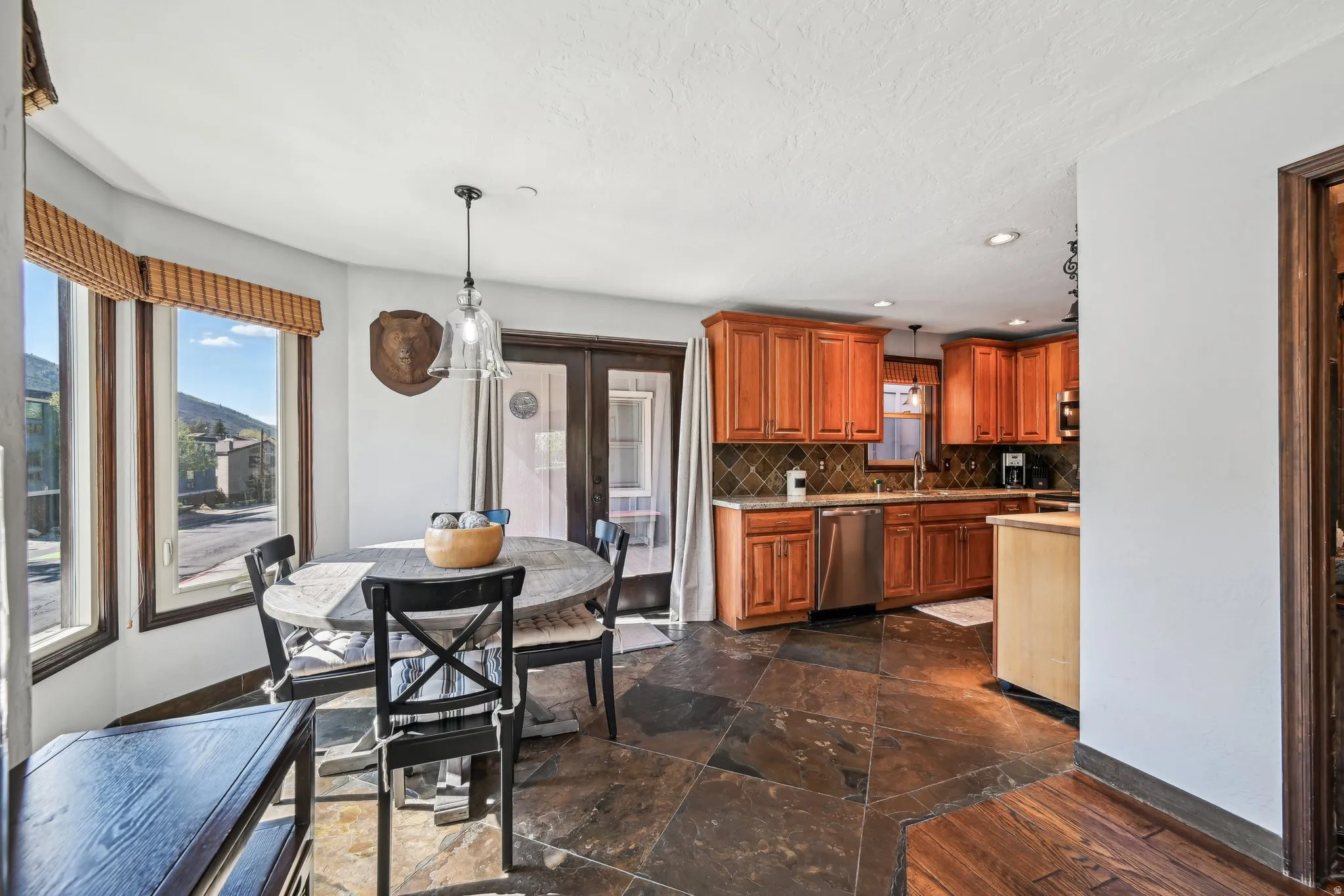 Kitchen featuring light countertops, decorative light fixtures, wood finish cabinets, stone tile flooring, and decorative backsplash