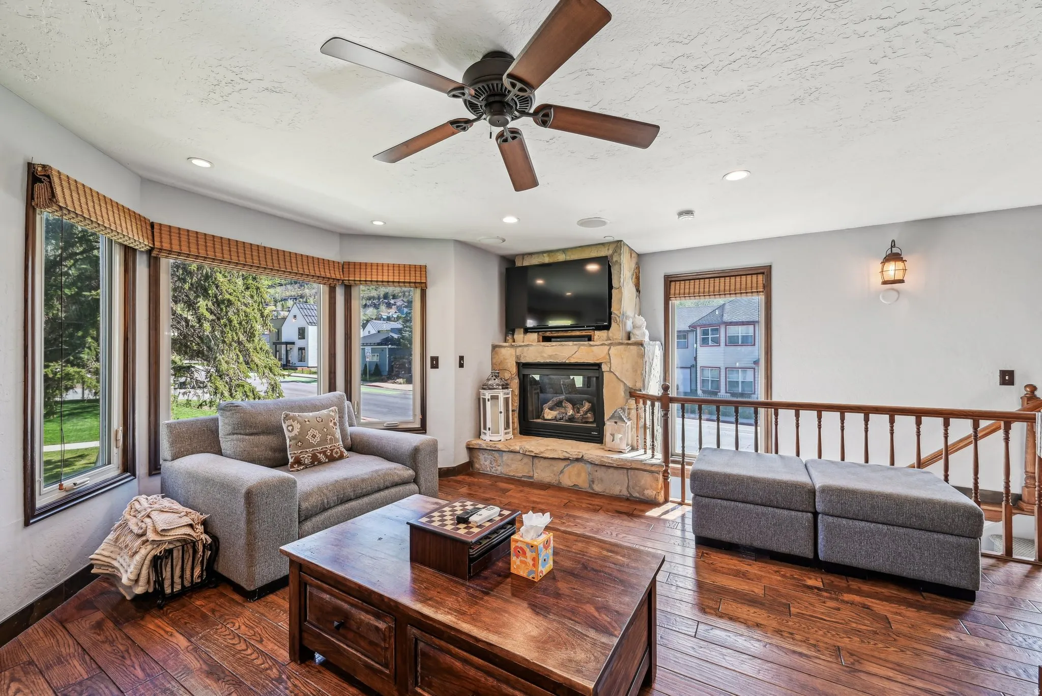 Living area featuring dark wood-style floors, a stone fireplace, a ceiling fan, a textured ceiling, and recessed lighting